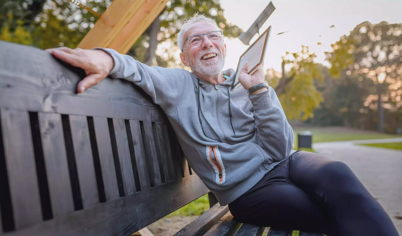 Aelterer Mann hoert Musik auf einer Parkbank